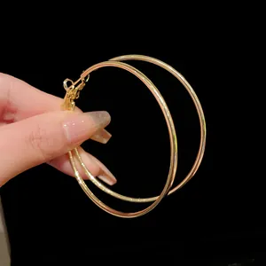 Detailed view of a pair of large minimalist gold-tone geometric metal hoop earrings.