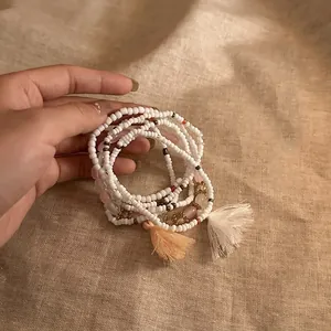 Close-up of handmade white beaded bracelet with pink quartz and tassels on linen.