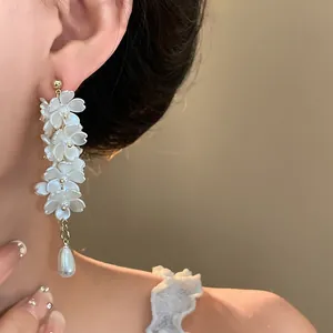 Close-up of elegant floral drop earrings with white resin petals and a teardrop faux pearl.