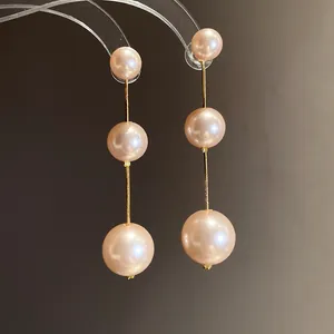 Detailed macro view of long drop earrings with three graduated pink pearls on a gold chain