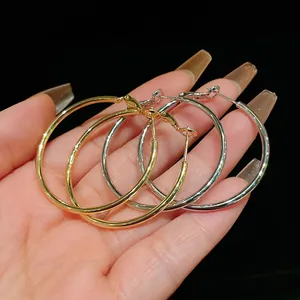 Detail view showing gold and silver minimalist metal hoop earrings held in hand for size.
