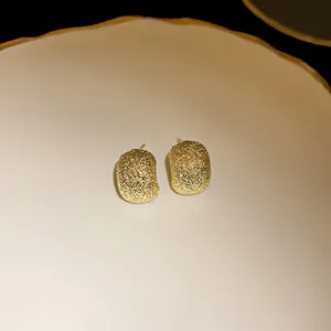 Close-up of golden irregular bean stud earrings with frosted glittery texture detail