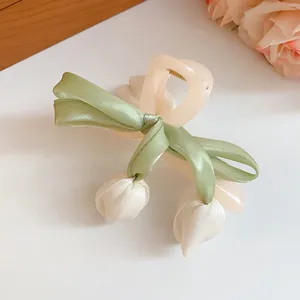 Elegant fabric tulip hair claw clip with a soft green ribbon bow on a white surface