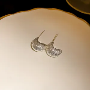 Macro view of textured silver crescent stud earrings on a white ceramic plate