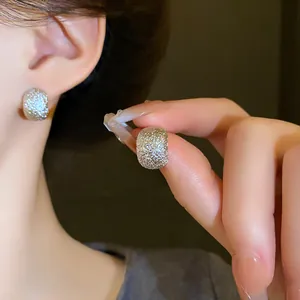 Close-up of irregular textured bean stud earrings with a sparkly glitter silver finish.