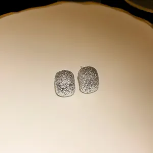 Close-up detail of silver irregular bean stud earrings with a frosted glitter texture