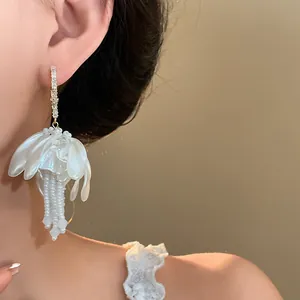 Detailed view of elegant white flower-shaped earring with pearl bead tassels worn by a model