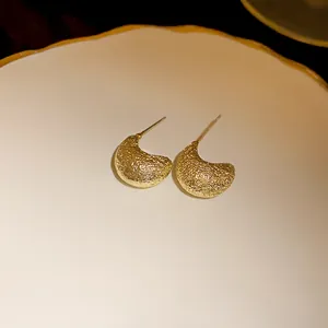Textured gold irregular bean stud earrings with silver needles detail macro view.