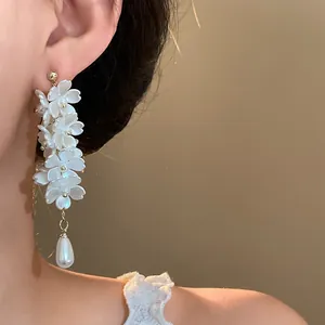Detail view of elegant white floral tassel earrings with pearl drop on model's ear