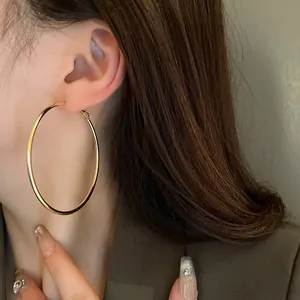 Close-up view of minimalist large gold metal hoop earrings worn on a female model's ear.