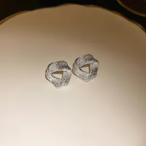Close-up of silver-toned irregular textured geometric stud earrings on a ceramic plate