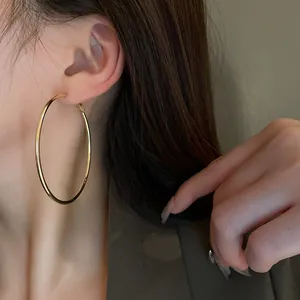 Close-up detail view of a minimalist large gold metal hoop earring worn on a model's ear