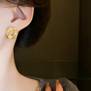 Close-up detail of a gold irregular geometric stud earring with textured finish on a model