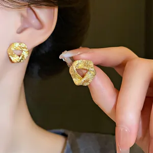 Close-up detail of irregular textured gold stud earrings featuring silver needle posts
