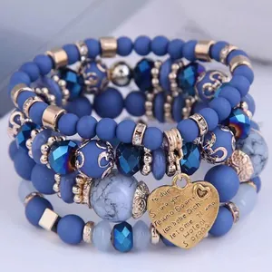 Close-up of multi-layer blue beaded bracelet stack with heart charm and 'I love you' engravings