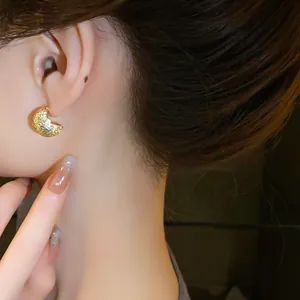 Close-up detail of textured gold crescent bean stud earring on female ear model