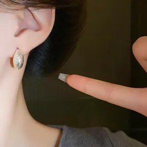 Close-up of a silver irregular bean earring with textured finish on a model's ear