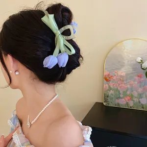 Detail of a purple tulip hair claw clip with green ribbon bows on a woman's bun.
