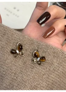 Close-up of butterfly stud earrings with faux tiger eye and zircon on beige knit