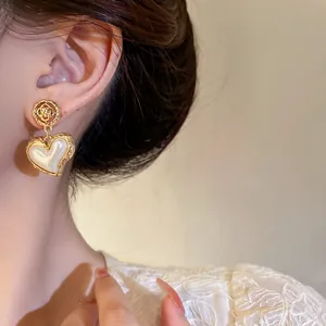 Close-up of elegant Baroque style gold heart earrings with pearl and floral details.