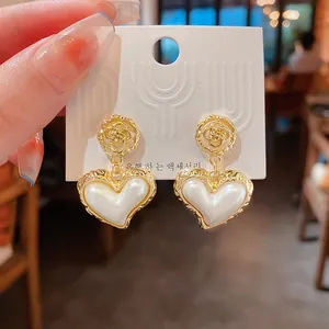 Close-up of Baroque style heart pearl earrings with wrinkled golden flower studs.