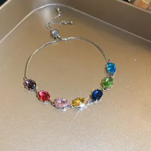 Adjustable silver bracelet with oval multi-colored zircons on a gold tray.