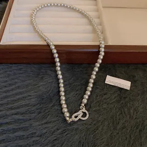Detail view of a pearl necklace with a crystal-encrusted geometric infinity clasp.