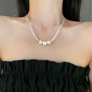 Close-up detail of a Baroque pearl pendant necklace on a minimalist multi-strand cord