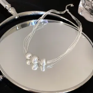 Close-up macro view of multi-strand silver necklace with three brushed metal beads on a mirror