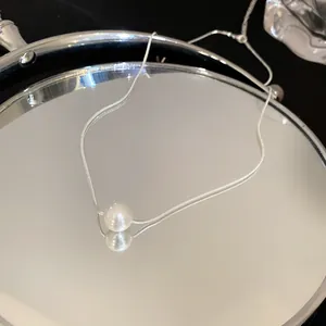 Elegant pearl pendant on a silver snake chain reflected in a round vanity mirror