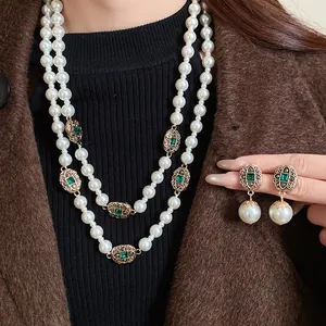 Macro detail of vintage style layered pearl necklace and earring set with green emerald gems.
