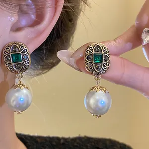 Macro view of vintage style drop earrings with green gems and white pearls