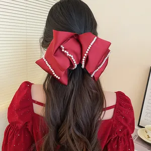 Large red satin bow hair clip with pearl trim for elegant festive hair styling.
