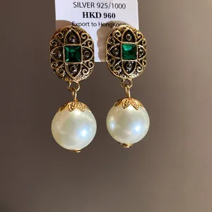 Macro detail of vintage-style gold earrings with emerald green crystals and large round pearls.
