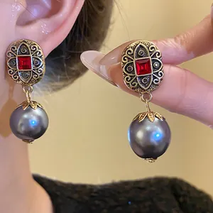 Macro detail view of vintage gold-tone drop earrings featuring red stones and grey pearls.