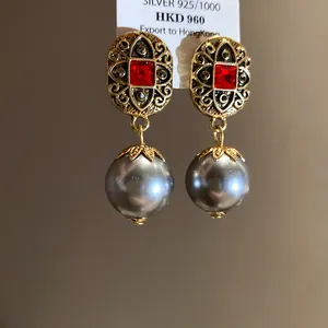 Close-up of vintage gold earrings with red stones and grey pearl drops on a silver tag.