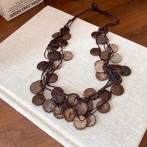 Boho chic necklace with irregular circular coconut shell discs and brown cord tassels.