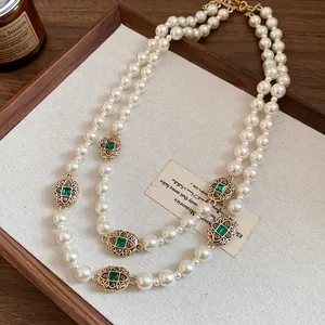 Close-up detail of vintage double-strand pearl necklace with emerald green gemstone accents