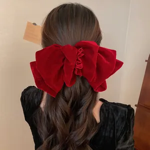 Detailed view of a large red velvet bow hair clip worn on long wavy brown hair.