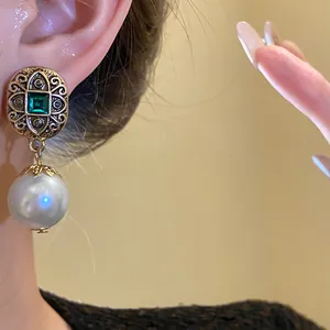 Detailed view of vintage gold stud earrings with emerald green stone and white pearl drop