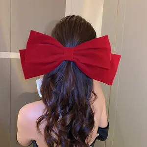 Detail view of an elegant large red velvet bow hair clip worn on a model's dark hair.
