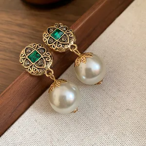 Close-up of vintage gold drop earrings with emerald green gems and white pearls.