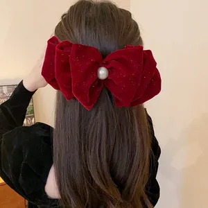 Detailed view of a festive red velvet bow hair clip with a pearl center on brown hair