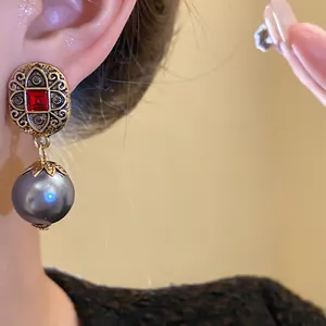 Close-up of vintage-style gold earrings with red stone and grey pearl drop