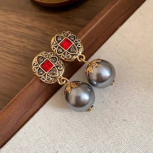 Detail view of vintage style earrings featuring red rhinestones and grey pearl dangles