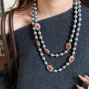 Macro detail showing vintage grey pearl necklace with ornate red gemstone accents on model