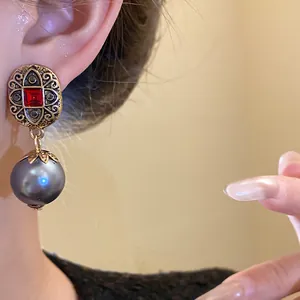 Close-up detail of vintage-style gold earrings with red stone and grey pearl pendant