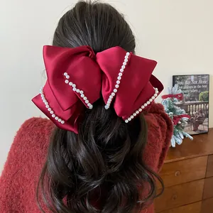 Close-up of a large red satin bow hair clip with pearl trim worn on dark wavy hair.
