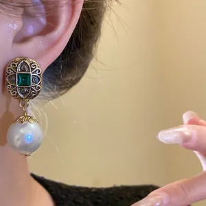 Detailed close-up showing a vintage gold filigree earring with green gemstone and pearl drop