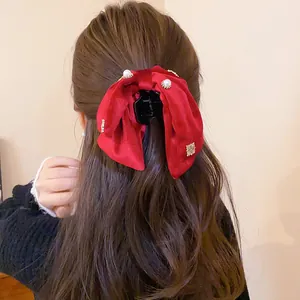 Macro detail view of a red velvet bow hair clip with pearls on a model's wavy hair.